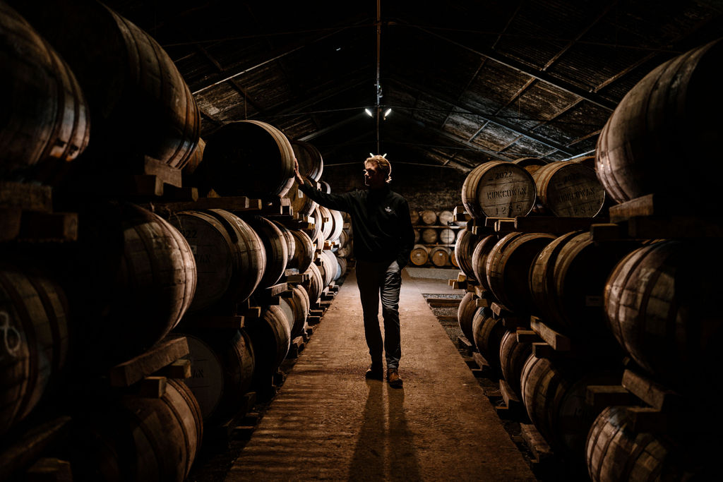A figure in a Bladnoch warehouse aisle between stacked casks