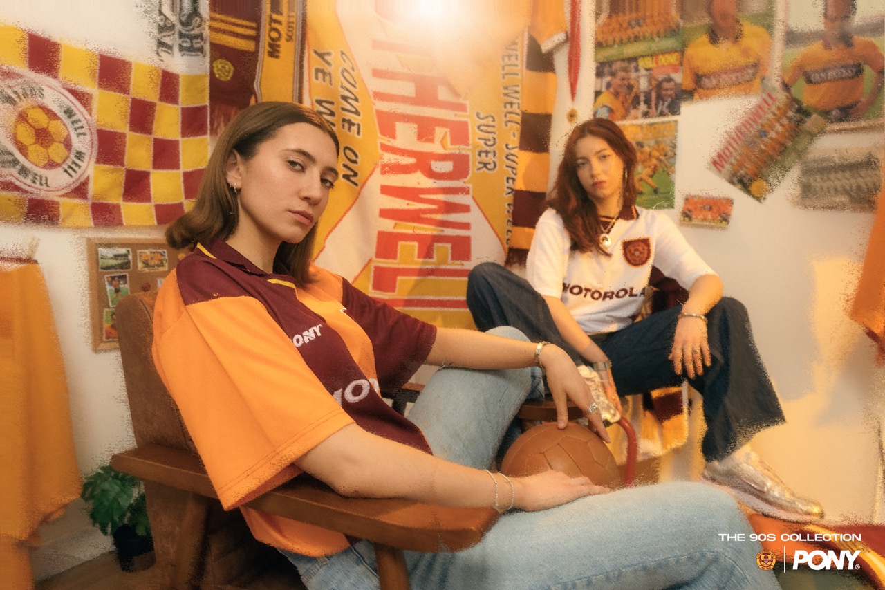 Two models in Motherwell FC 90s shirts in a room hung with scarves