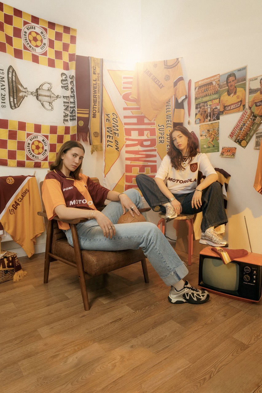 Two models in Motherwell retro kit in a room of old programmes