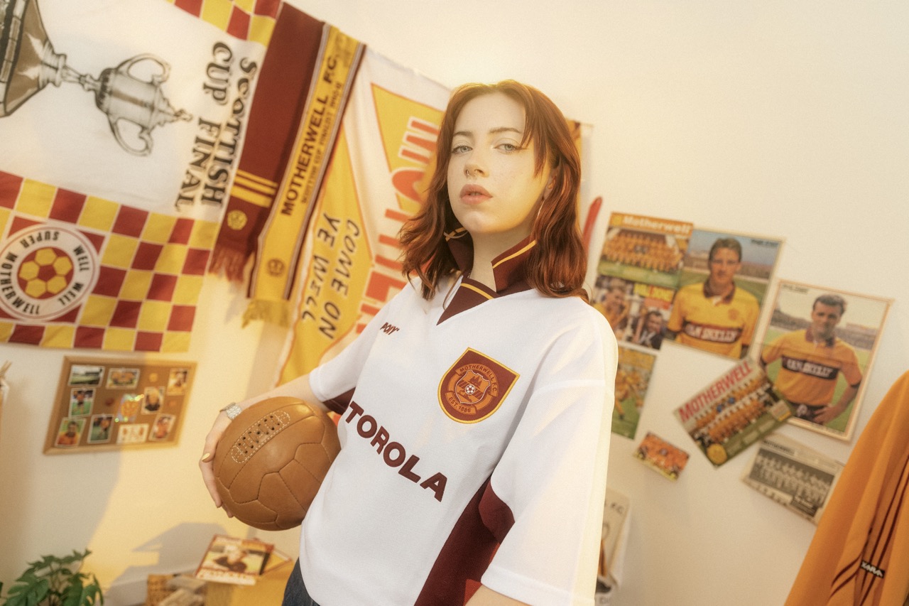 A model in the white Motherwell away shirt holding a football