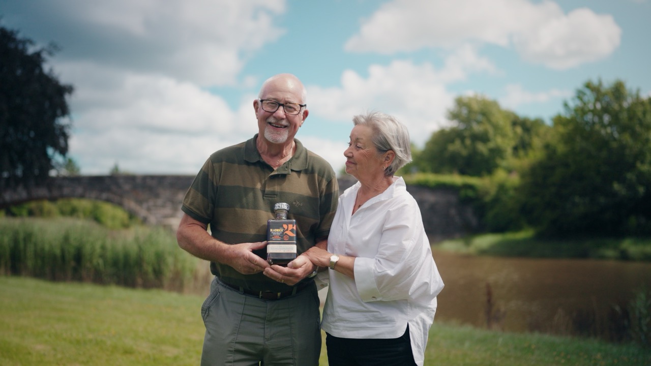 Roddy and Elaine holding a bottle of Bladnoch beside the river
