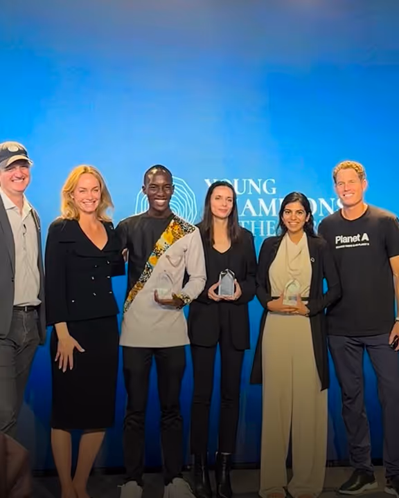 Six people stand on stage holding awards against a blue background with text about young champions.