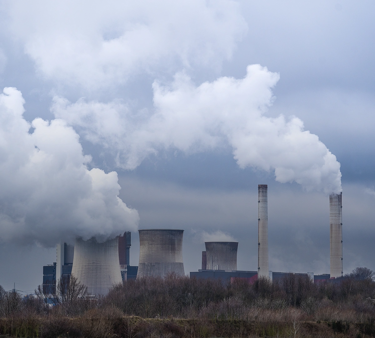 Industrial power plant with cooling towers and chimneys emitting thick white smoke under a cloudy sky.