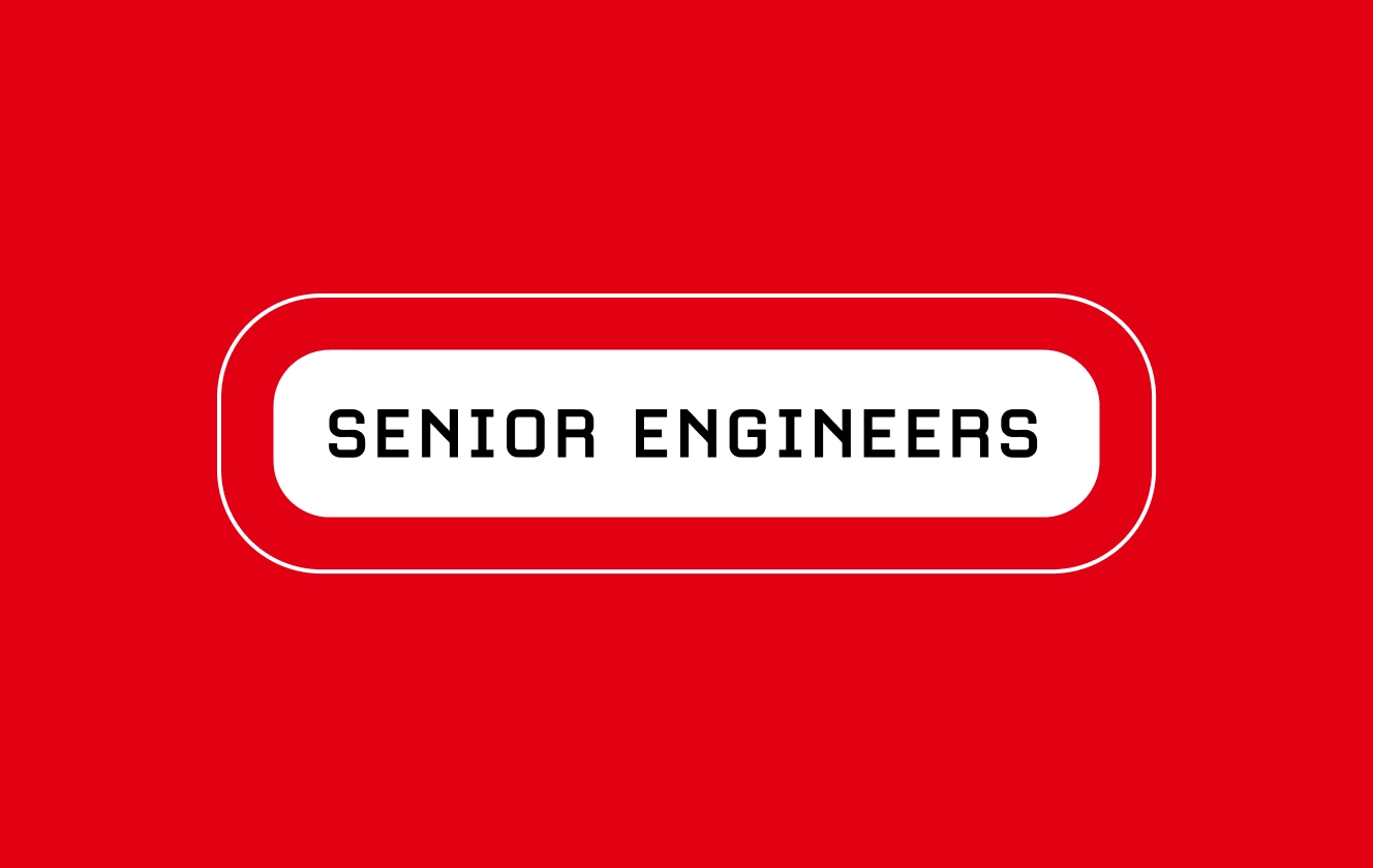 two male senior software developers looking at computer screens in a busy office