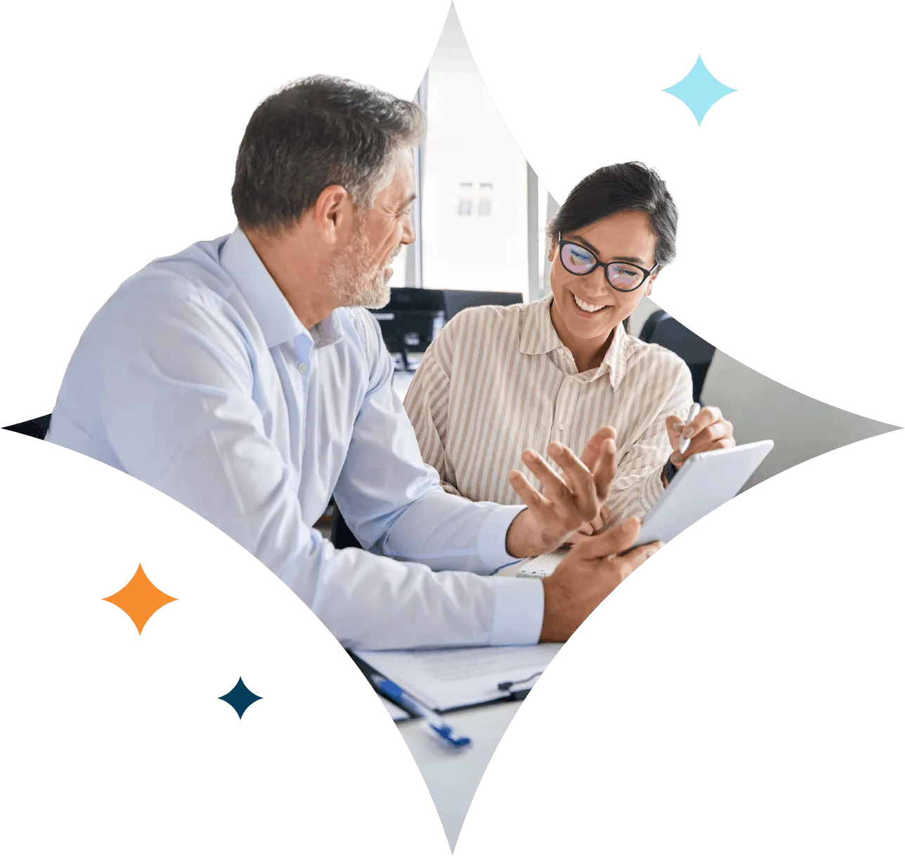 Two colleagues smiling and discussing work while looking at a tablet in an office.