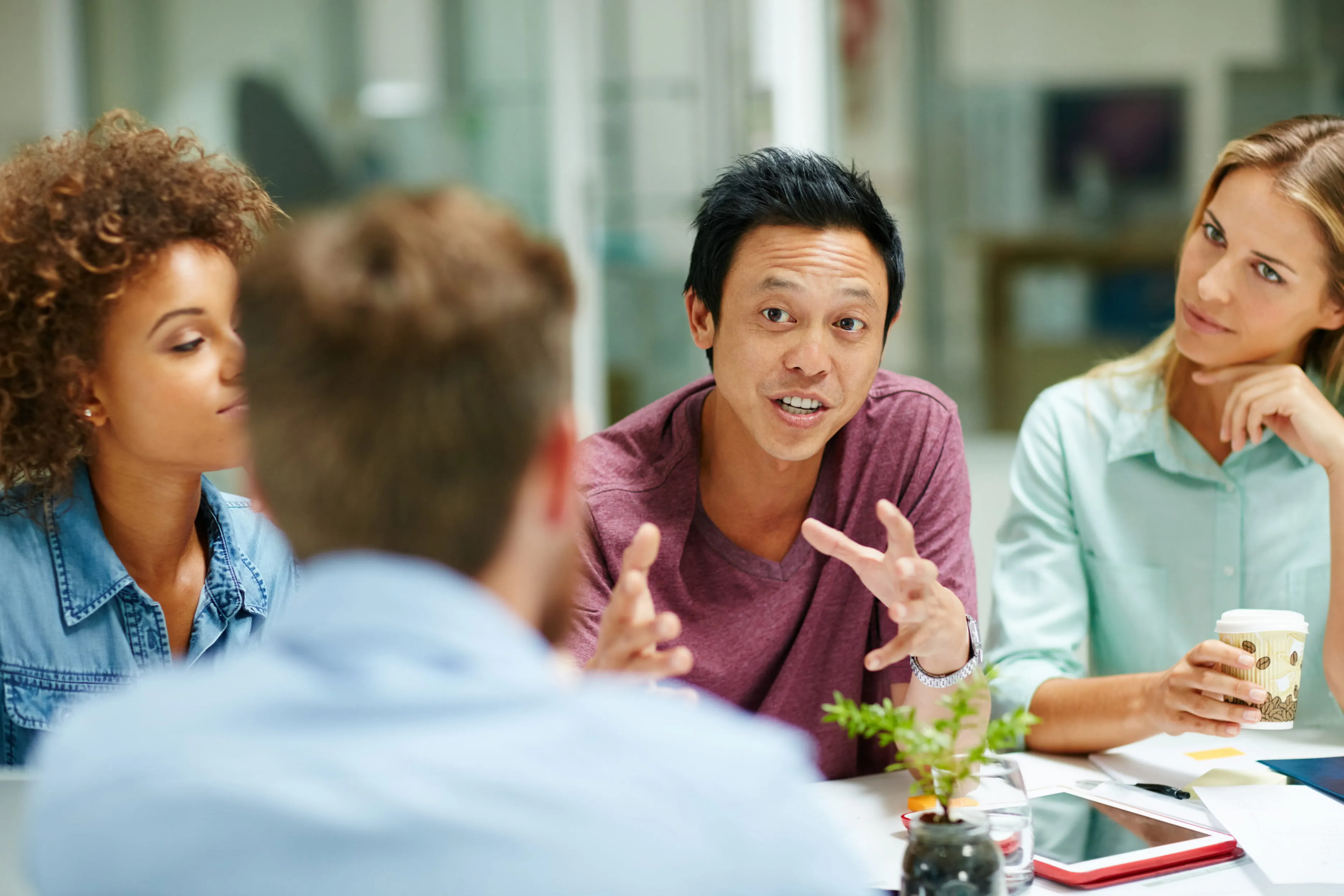 Four diverse colleagues engaged in a discussion around a table with digital devices and a coffee cup.