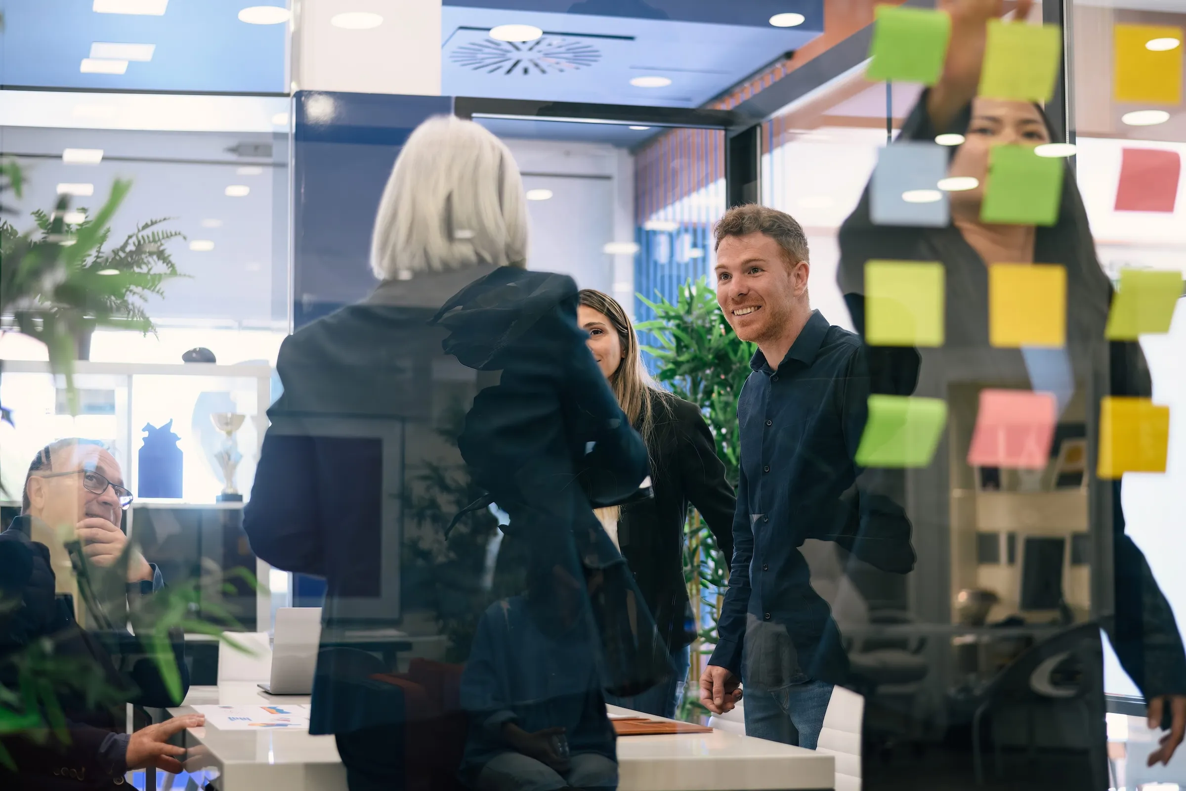 Business colleagues collaborating in an office with sticky notes on a glass wall during a meeting.