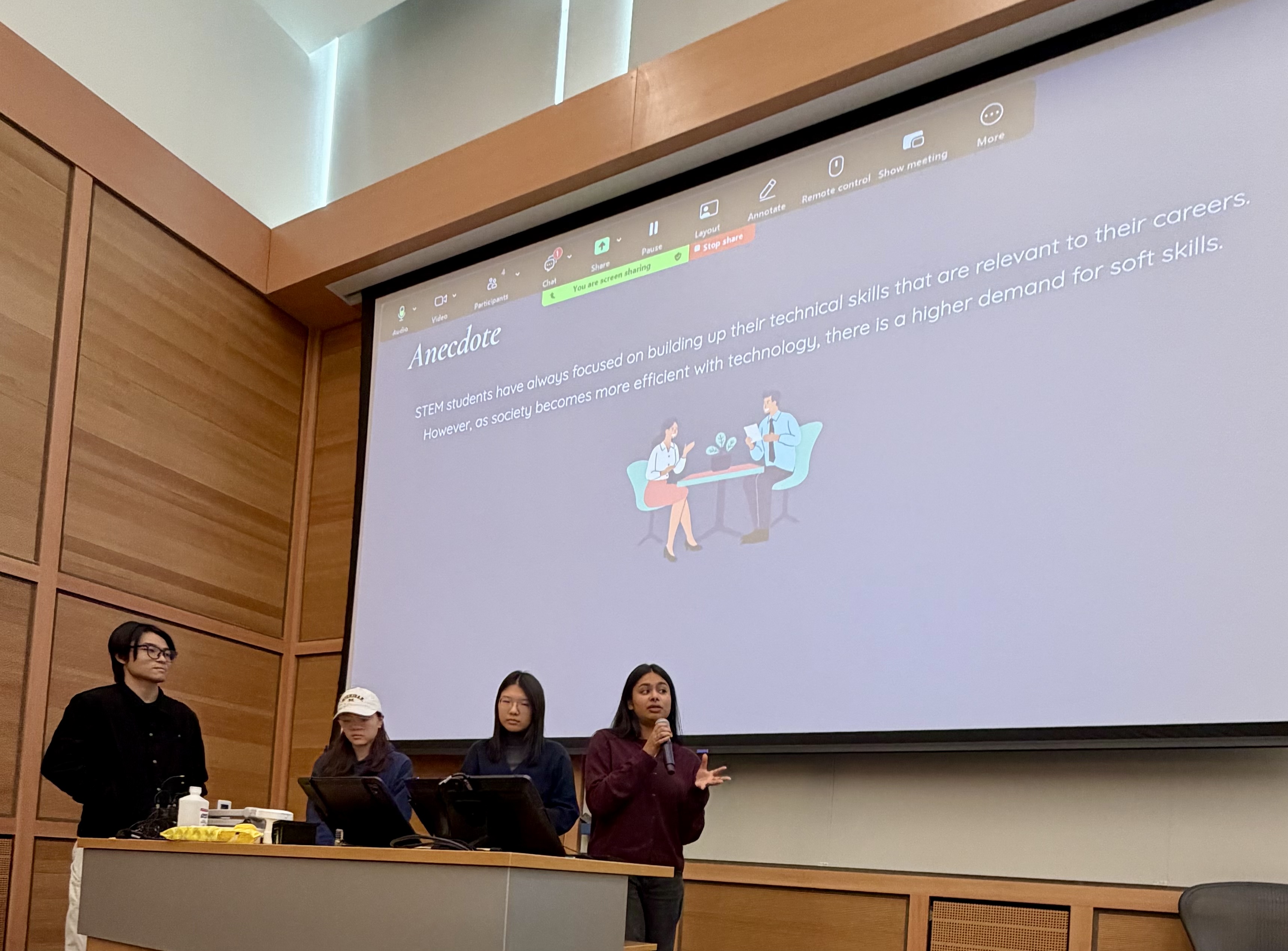 Sharanya and her three other team members presenting their presentation. On the big presentation board behind them is the anecdote they are opening up their presentation with. 
