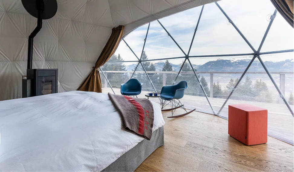 Chambre de pod avec lit et fauteuils face à la paroi vitrée – Whitepod, hôtel insolite dans les Alpes suisses