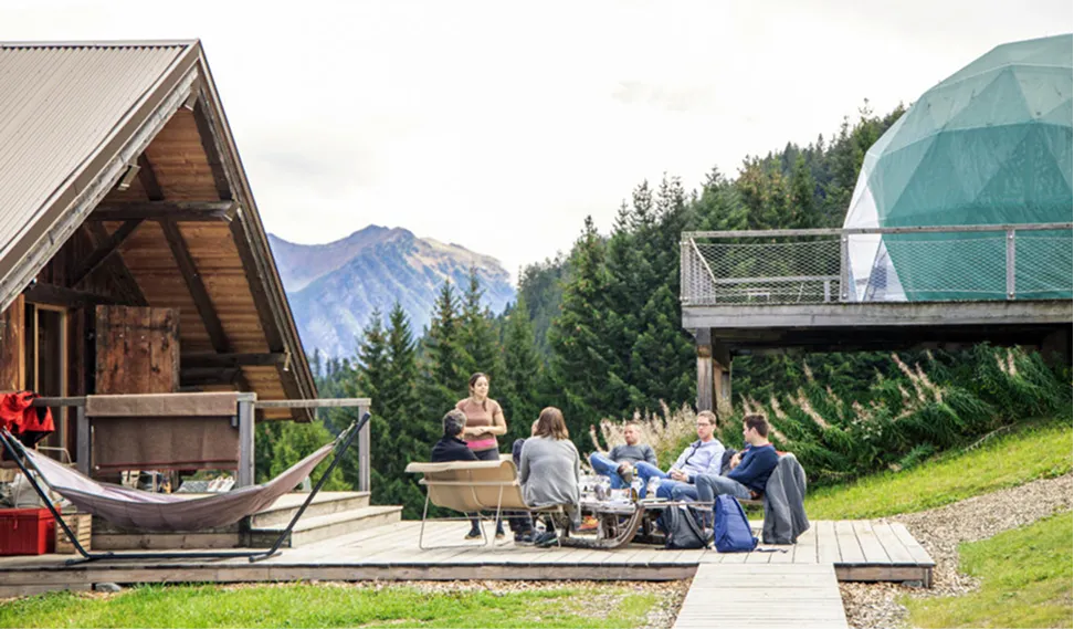 Convives sur la terrasse entre un chalet et un pod – Whitepod, hôtel insolite dans les Alpes suisses