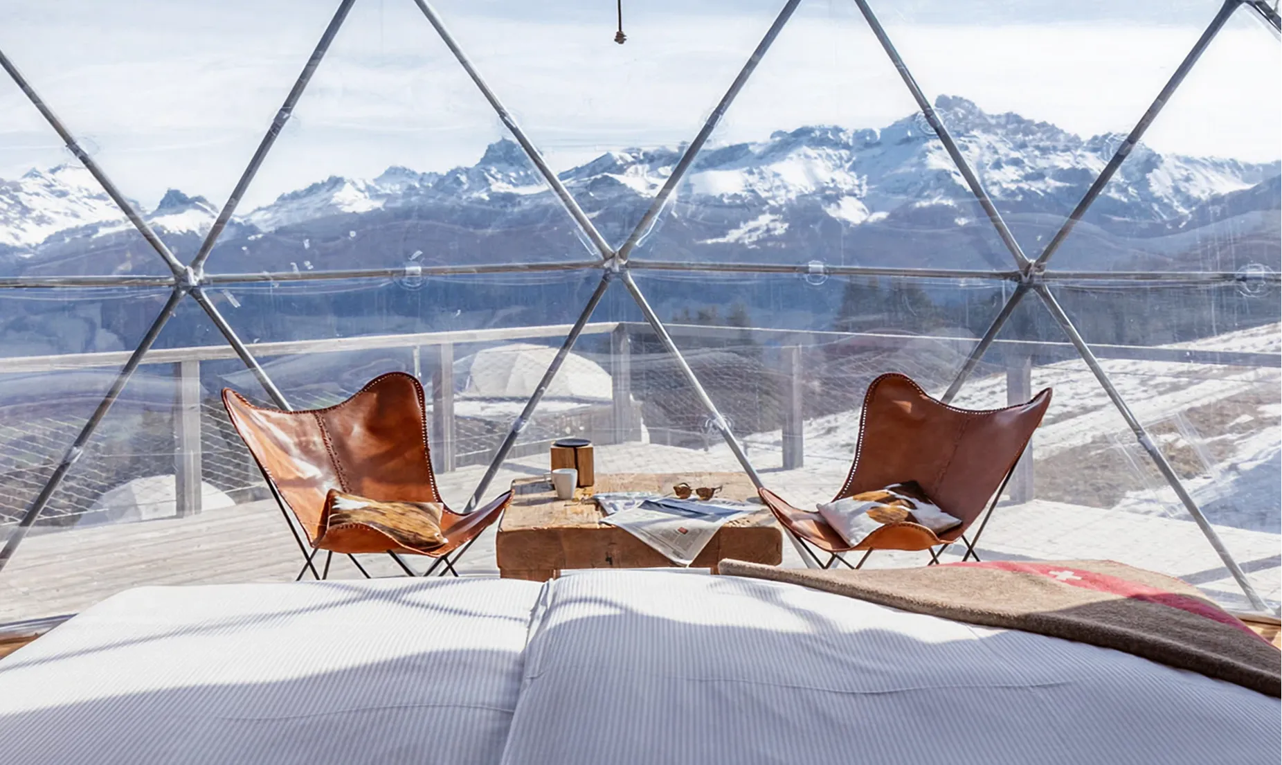 Intérieur d'un pod transparent avec deux fauteuils en cuir face aux sommets enneigés – Whitepod, hôtel insolite dans les Alpes suisses