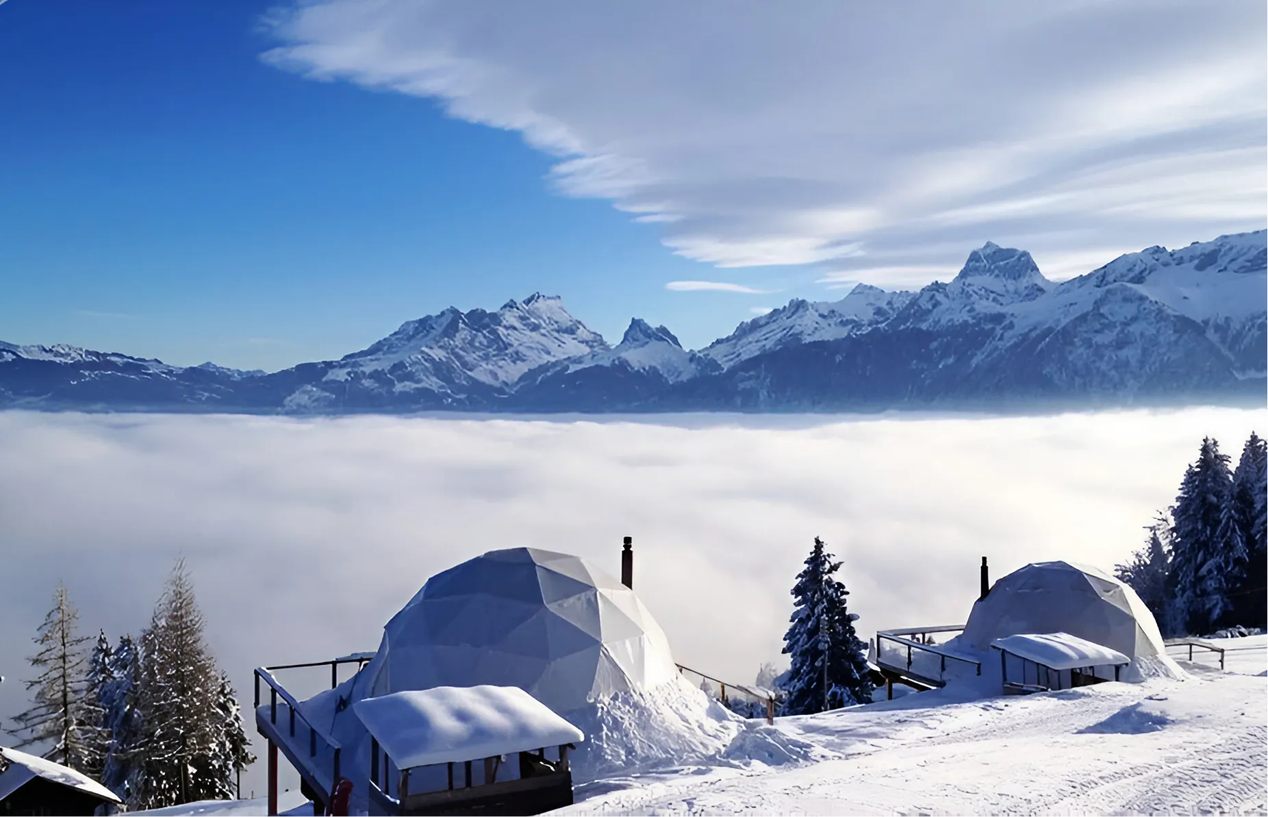 Zwei verschneite Pods vor Nebelmeer und Alpengipfeln – Glamping in Kuppeln im Whitepod im Wallis