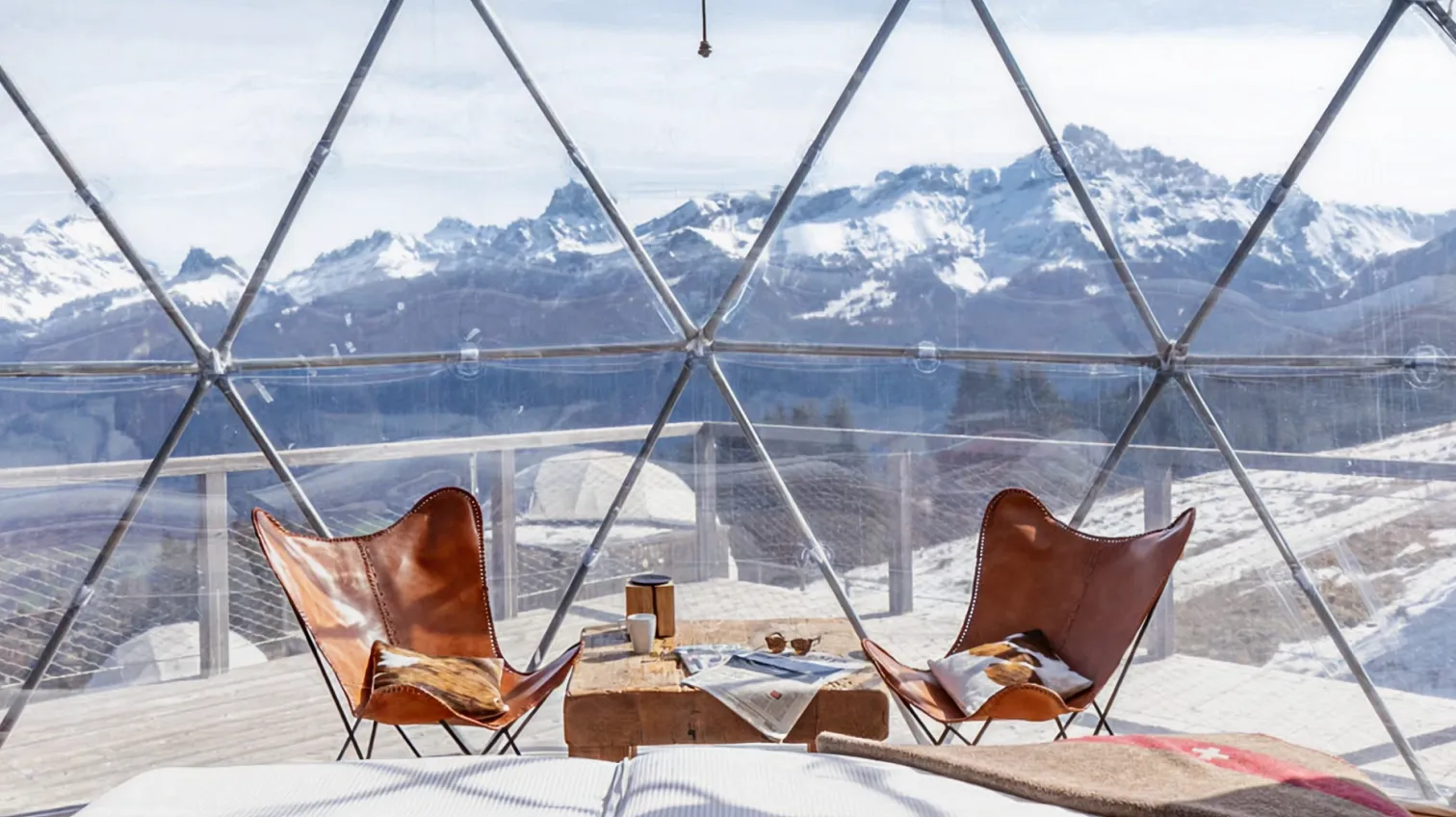 Zwei Ledersessel in einem verglasten Pod mit Blick auf verschneite Gipfel – Glamping in Kuppeln im Whitepod im Wallis