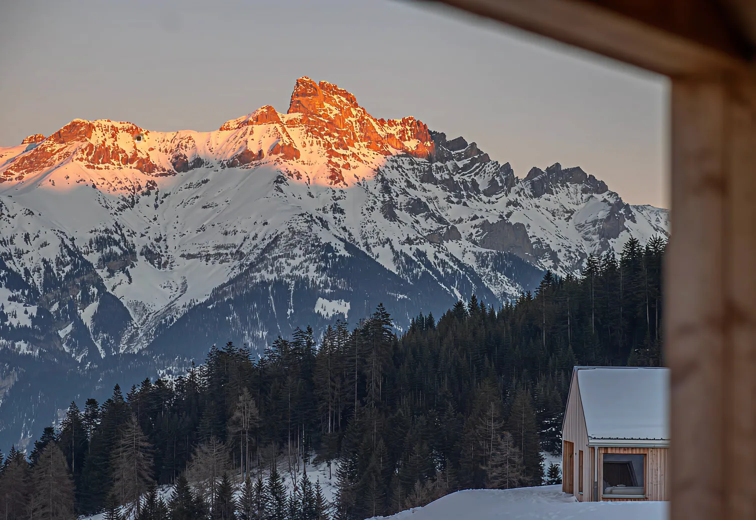 Sommets enneigés rosis par le coucher du soleil vus depuis la fenêtre d'un chalet – chalet Whitepod à louer dans le Valais