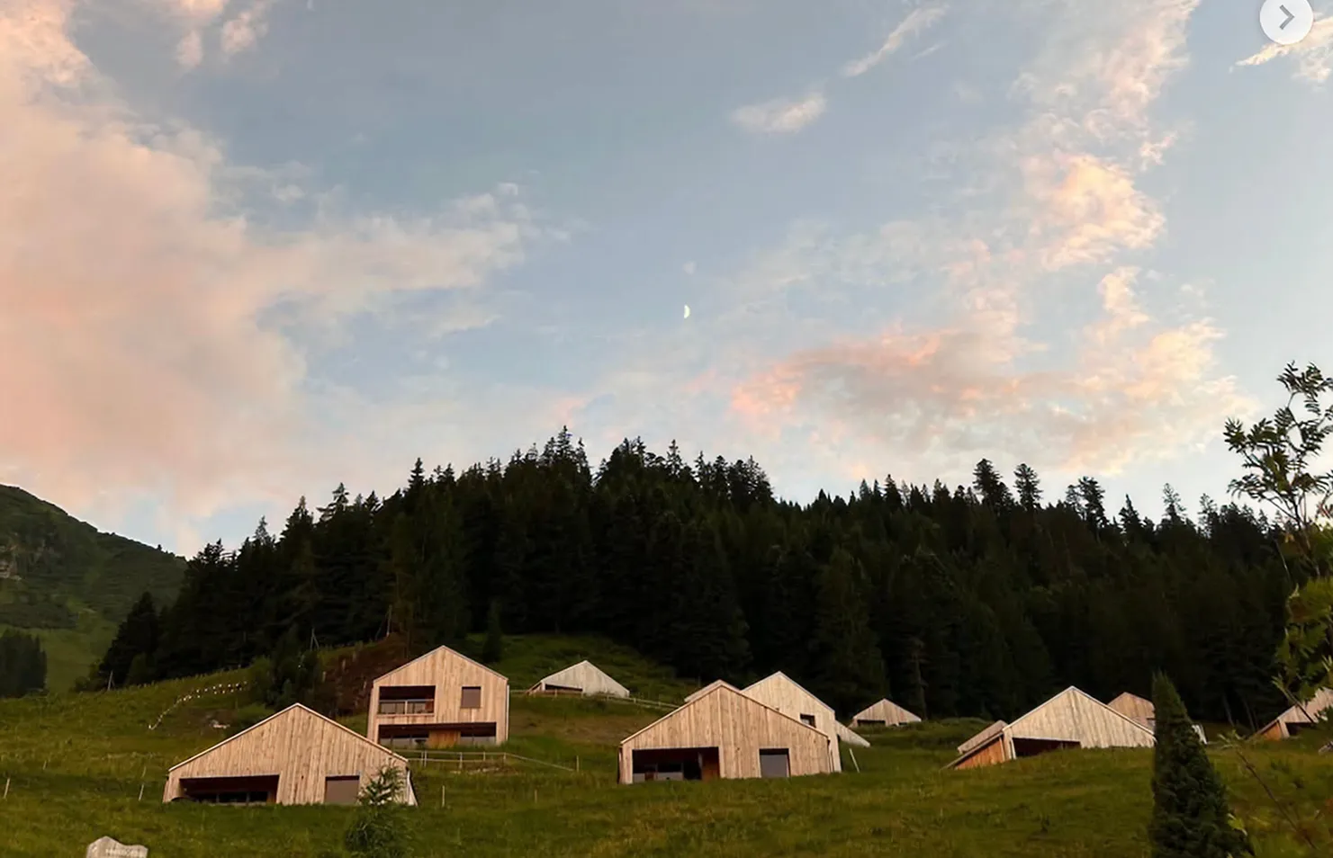Chalets en bois dispersés sur un alpage au crépuscule – chalet Whitepod à louer dans le Valais