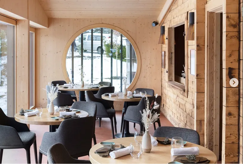 Speisesaal mit rundem Bullauge und gedeckten Tischen vor der Schneelandschaft – Bergrestaurant Les Cerniers oberhalb von Monthey