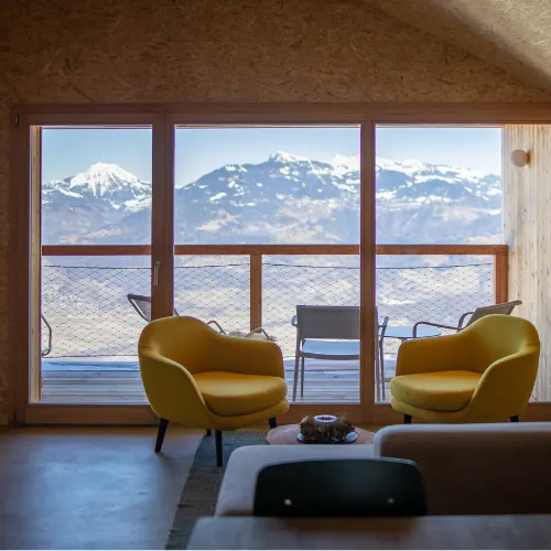 Salon avec fauteuils jaunes devant une baie vitrée sur les montagnes – Chalet Cosy, chalet Whitepod dans le Valais