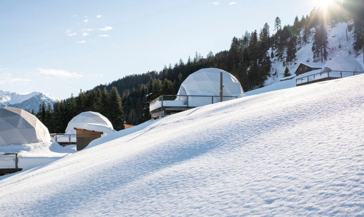 Pods en dôme sur une pente enneigée baignée de soleil – Elle présente les igloos de Whitepod en Suisse