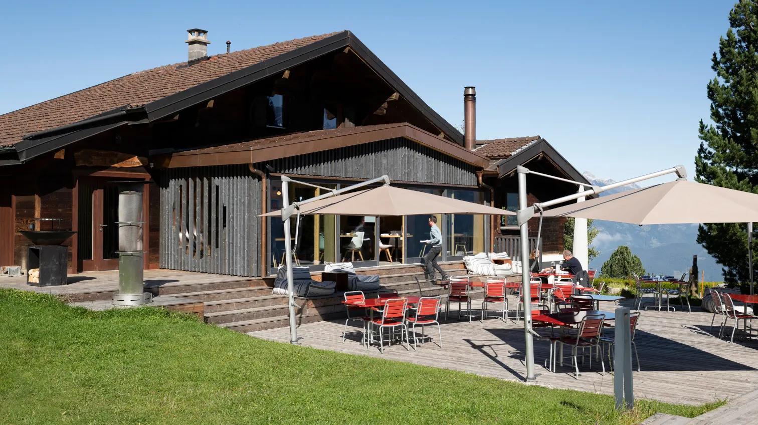 Terrasse ensoleillée avec parasols devant un grand chalet en bois – restaurant Les Cerniers au-dessus de Monthey