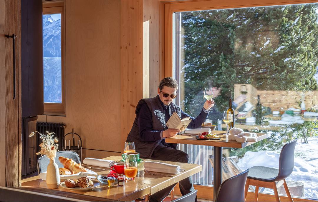 Client attablé devant un brunch dans une salle vitrée face aux sapins – restaurant Les Cerniers au-dessus de Monthey