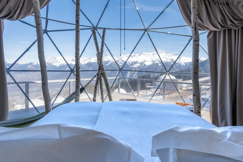 Bett vor der Glaswand mit Blick auf verschneite Gipfel – Forest Pod Suite, Pod von Whitepod im Wallis