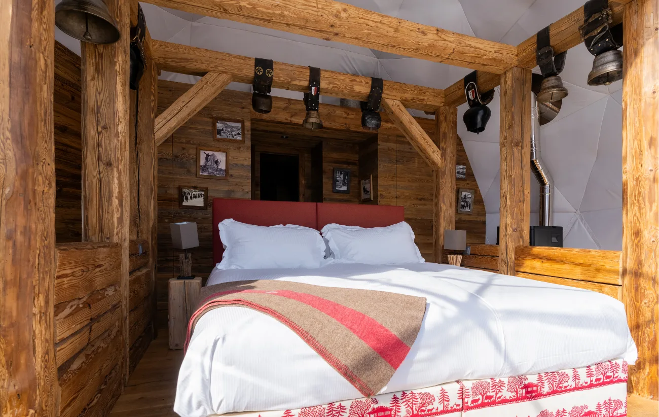Altholzbett mit gestreifter Decke unter dem Gebälk einer Suite – Pod Suite Schweiz, Pod von Whitepod im Wallis