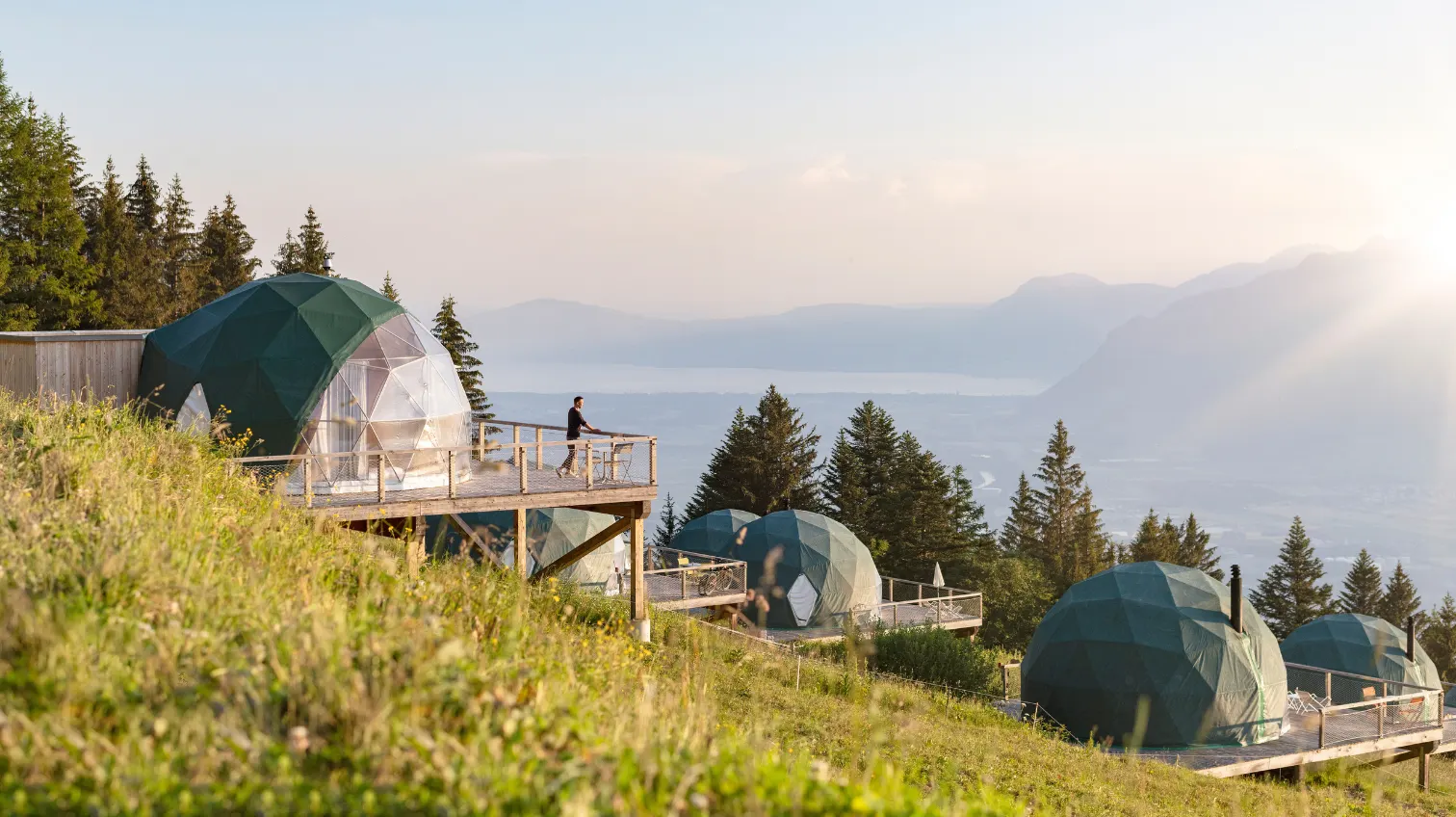Pods en dôme sur une pente herbeuse face à la vallée au lever du soleil – Whitepod, hôtel insolite dans les Alpes suisses