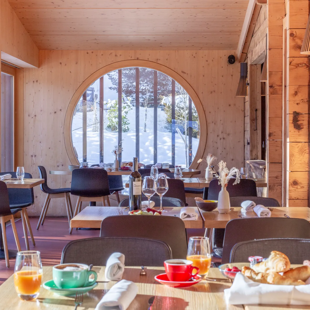 Salle au hublot rond avec tables dressées face au paysage enneigé – restaurant Les Cerniers au-dessus de Monthey
