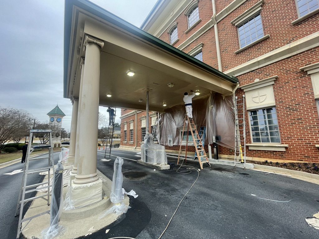 Construction workers on ladders performing maintenance on the covered entrance of a red brick building.