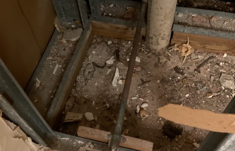 Exposed dirt floor with debris and metal framing inside a construction or demolition site.