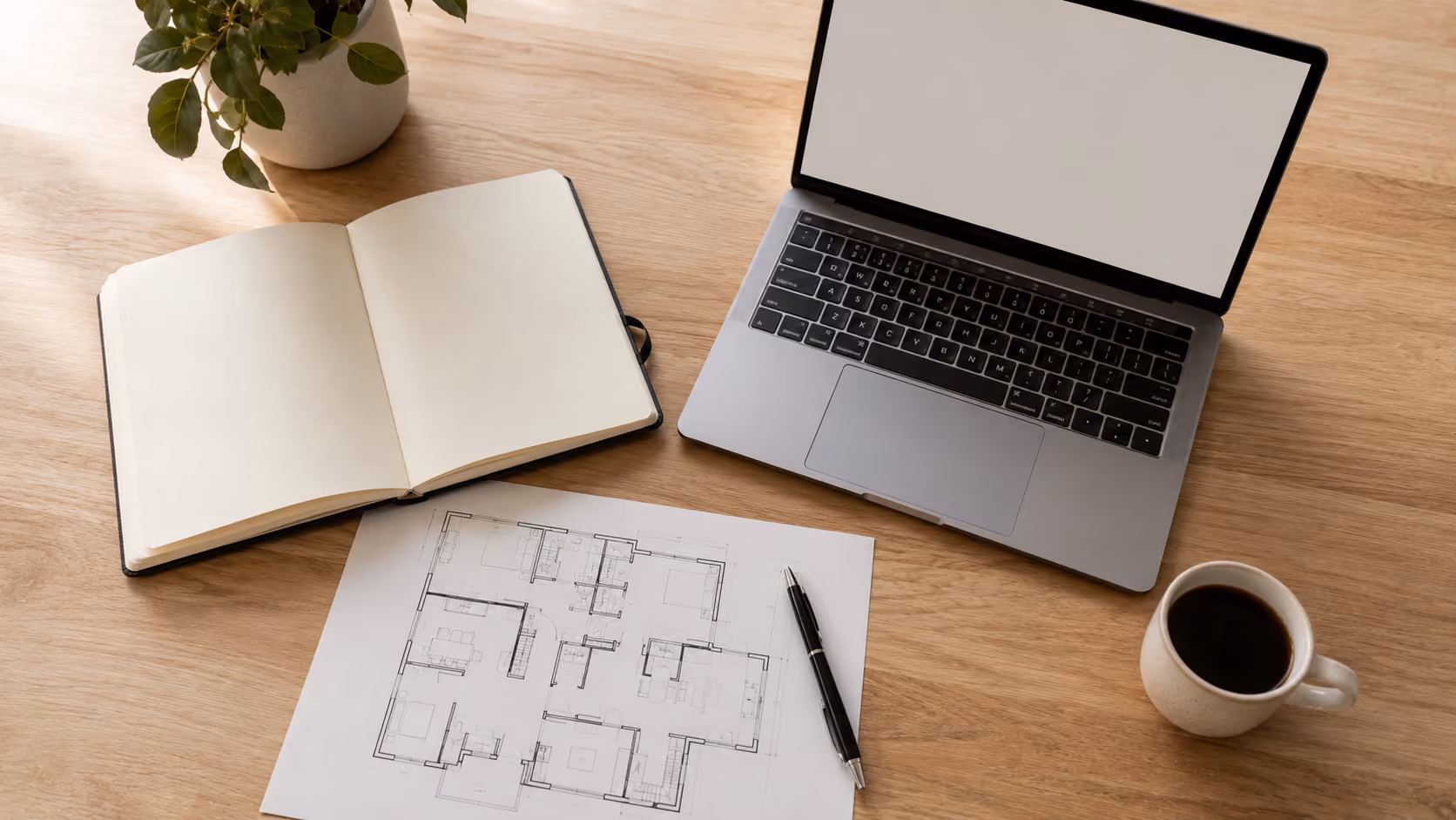 Table de travail avec un carnet, un plan d'étage et un ordinateur portable illustrant la révision d'une stratégie de mise en marché immobilière
