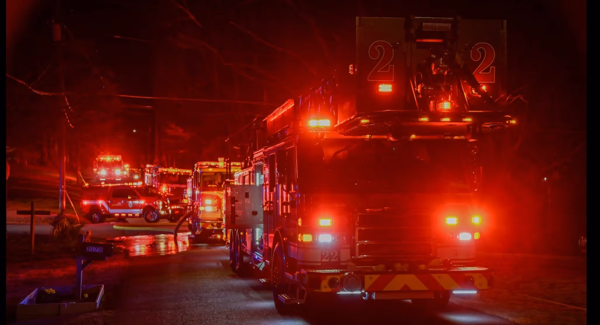 Fire trucks and emergency vehicles with flashing red lights at night on a street.