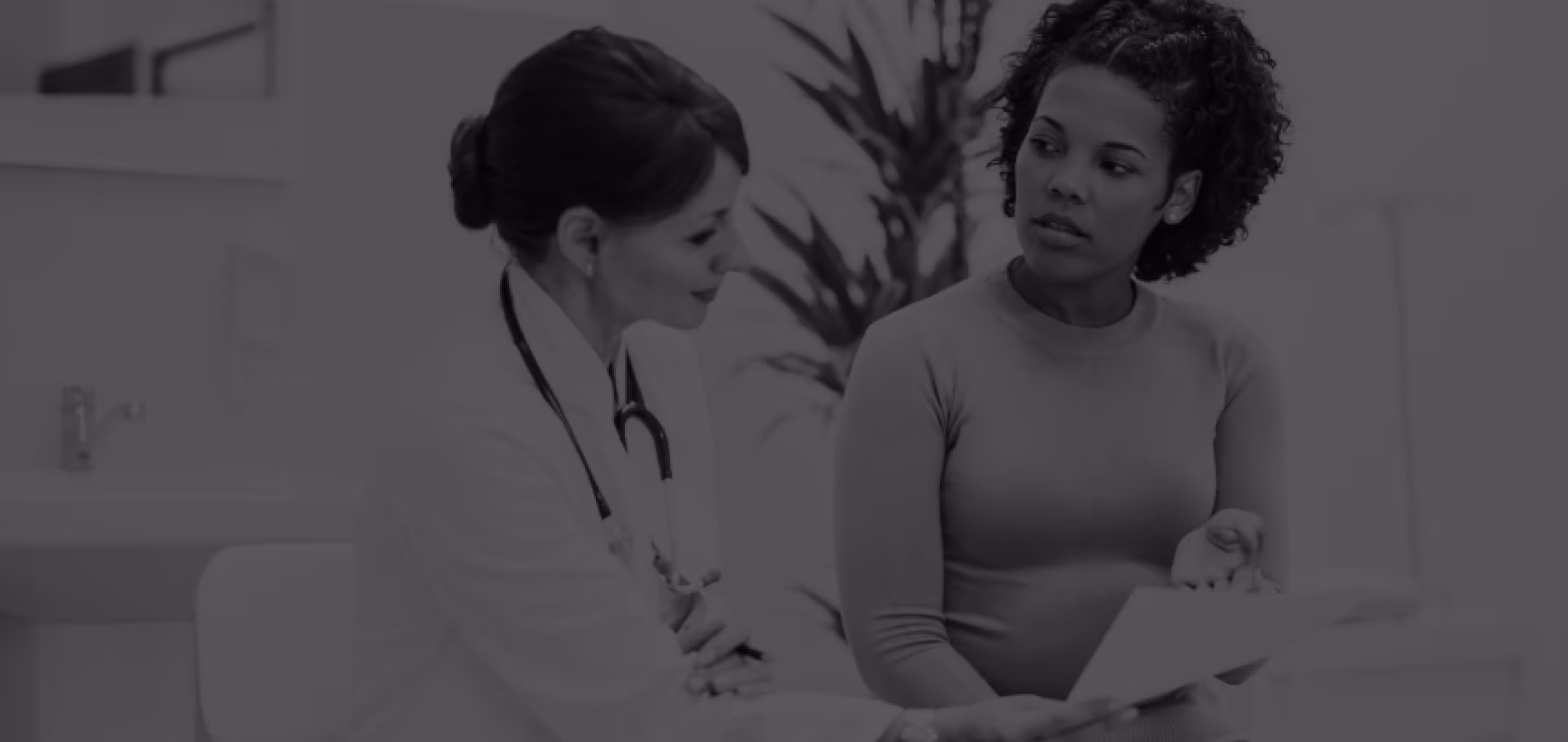 Doctor discussing medical information with a pregnant woman holding a clipboard in a clinical setting.