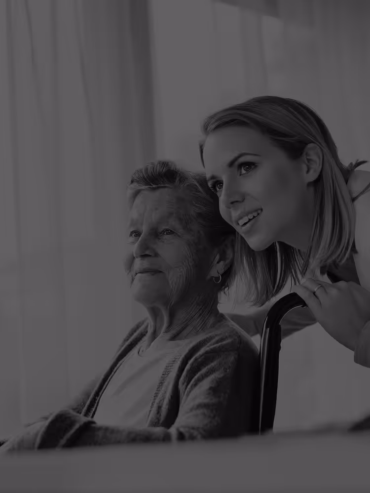 Elderly woman sitting with a younger woman leaning beside her, both looking content and smiling.