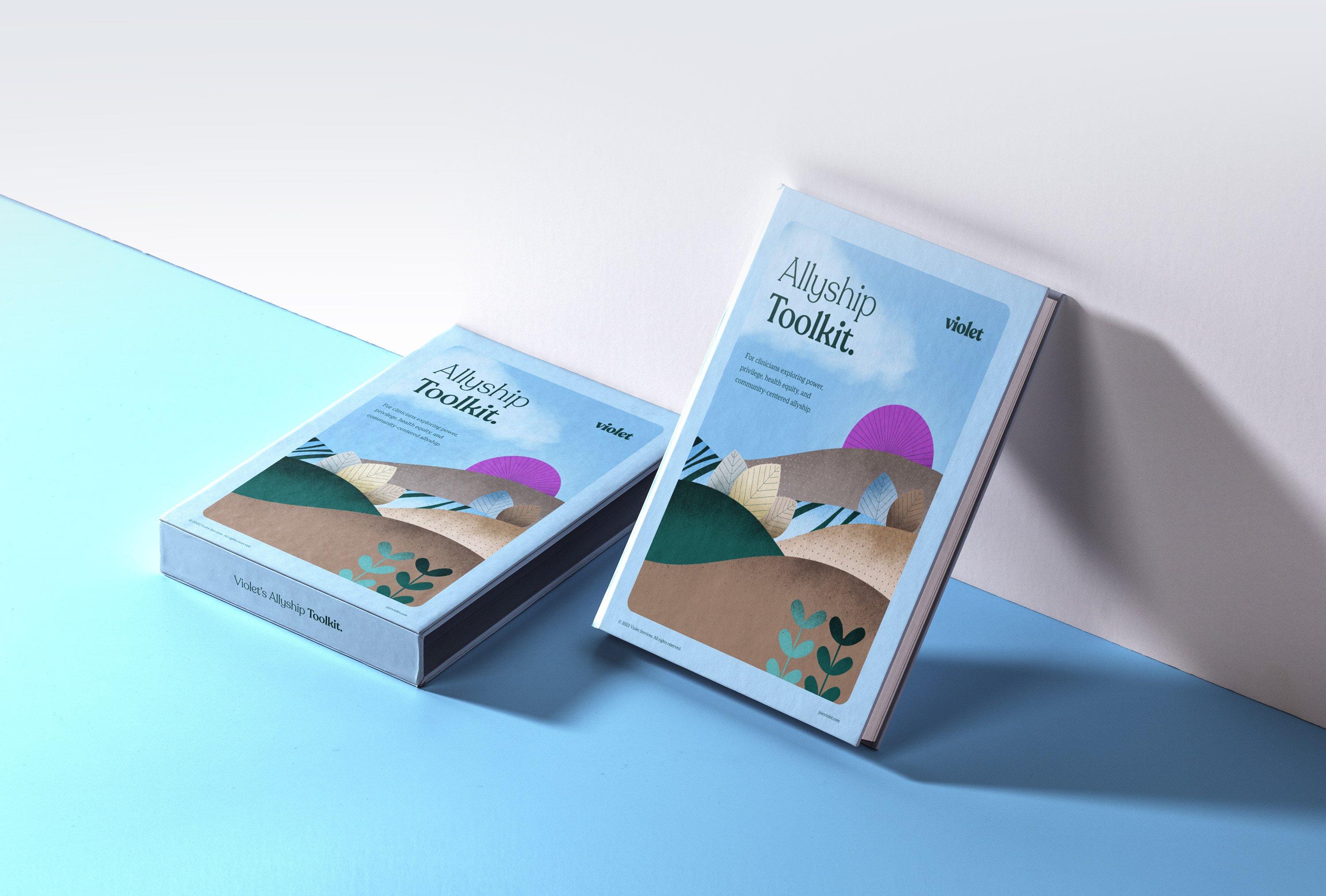 Two copies of the Allyship Toolkit by Violet, one lying flat and one standing, with an illustrated landscape cover showing hills, leaves, and a purple sun.