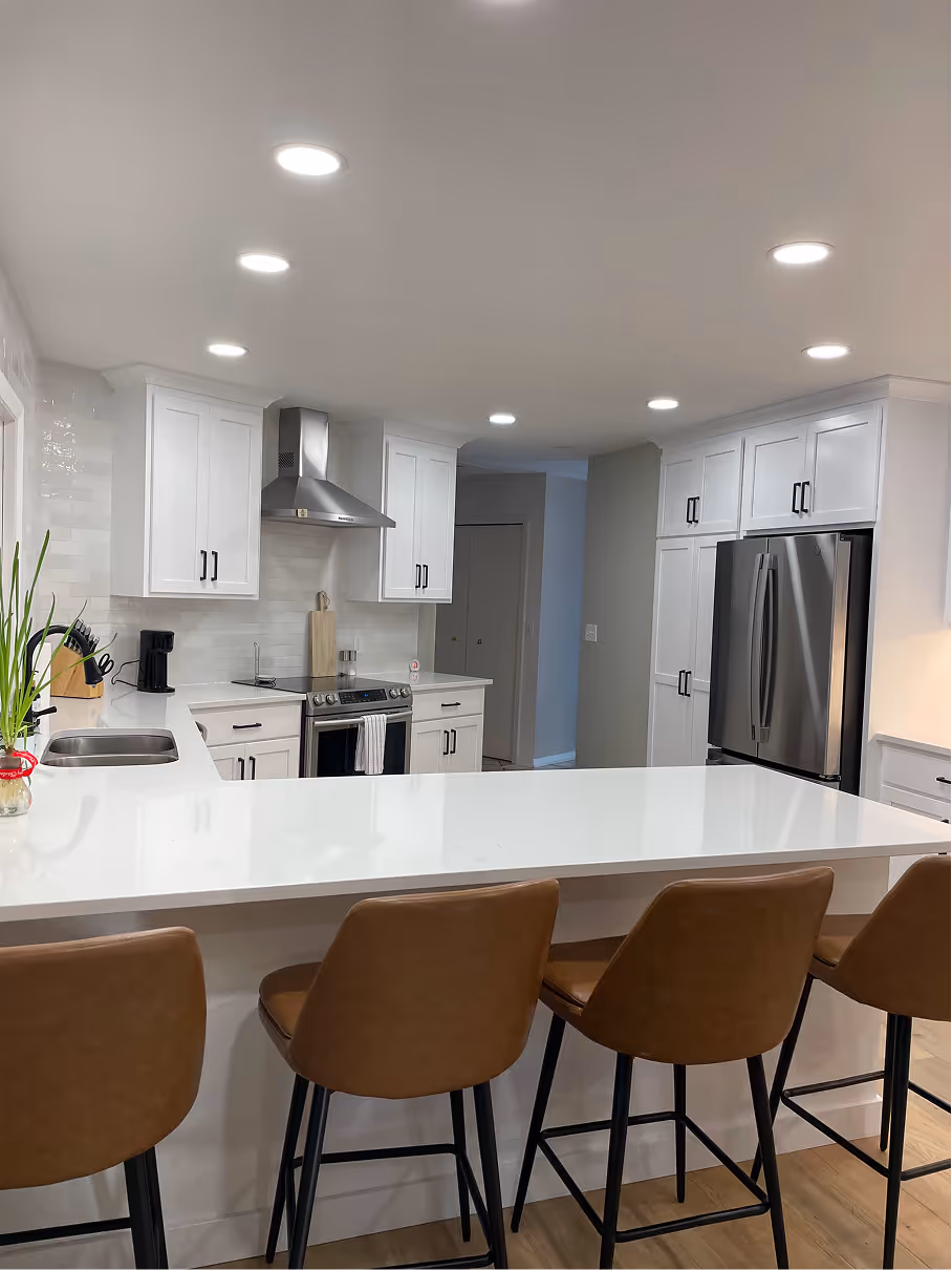 Kitchen wall with full-height white cabinetry, stainless steel refrigerator, under-cabinet lighting, and wood floors.