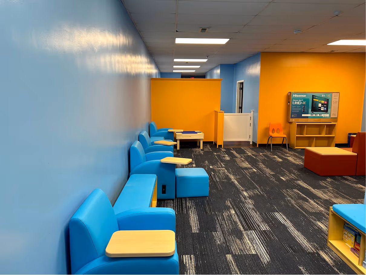 Children’s common area with blue and yellow walls, carpet flooring, modular seating, and activity furniture.
