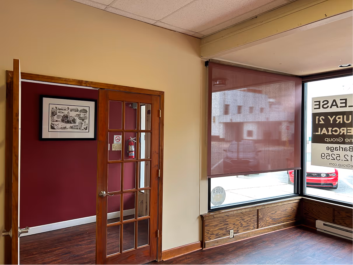 Interior office space before renovation with beige walls, carpet flooring, and kitchenette in the background.