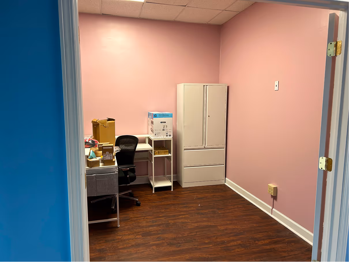 Finished office interior with pink accent walls, wood flooring, storage cabinets, and desk area.