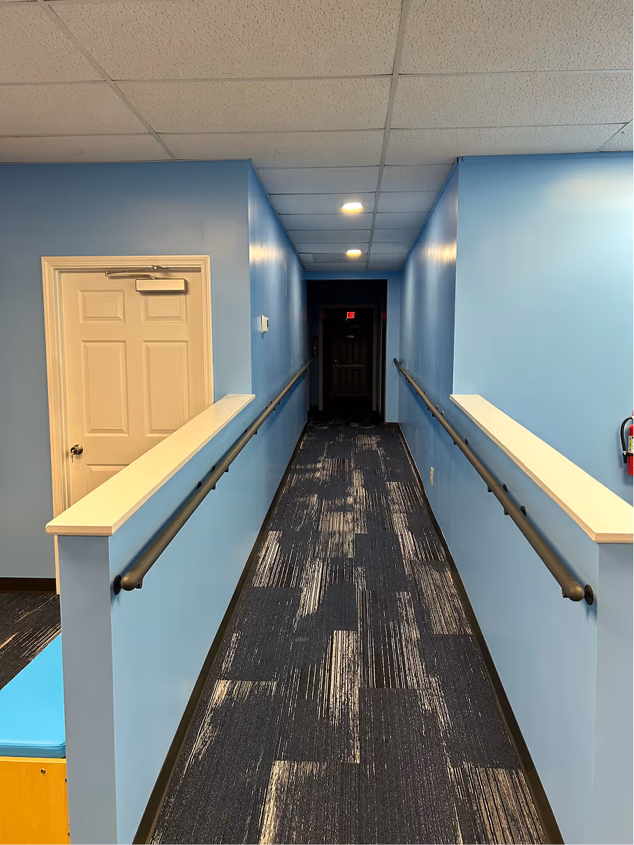 Interior hallway with blue painted walls, patterned carpet flooring, handrails, and recessed ceiling lighting.