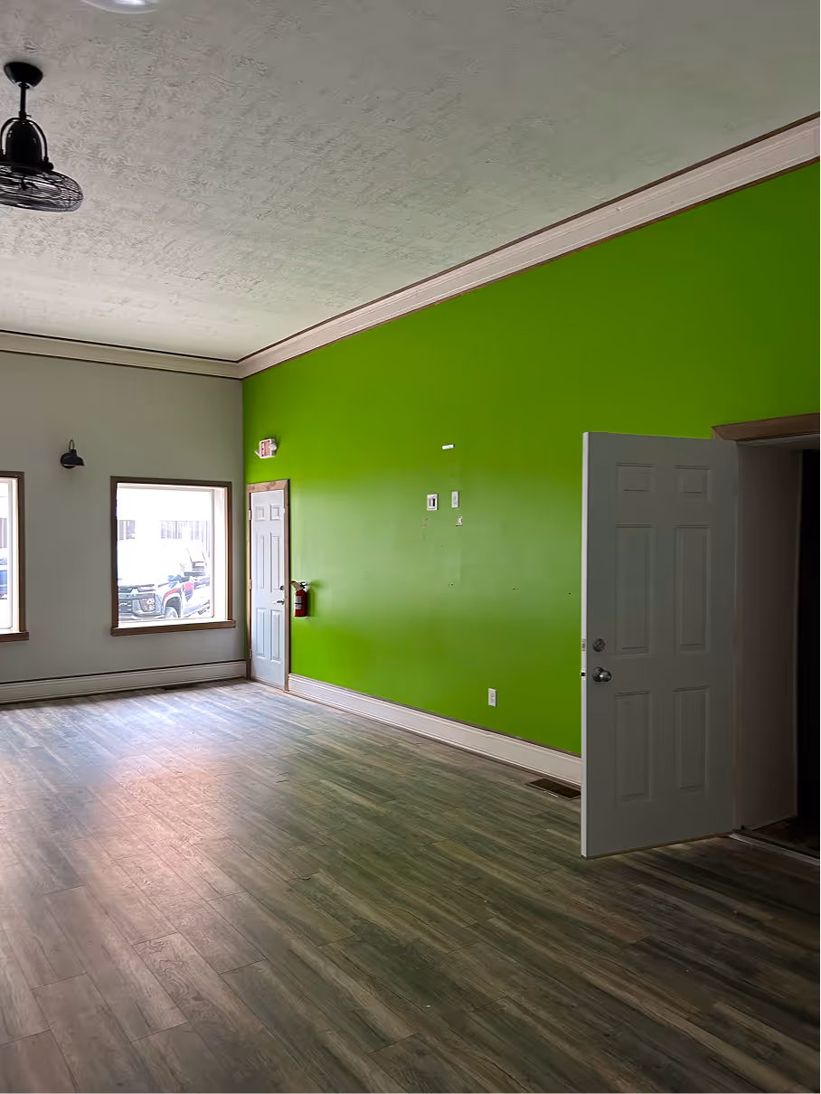 Existing commercial interior with green accent wall, wood-look flooring, and unfinished wall openings before renovation.