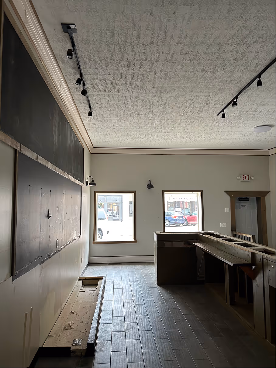 Front interior view showing service counter area, large windows, and unfinished wall surfaces before renovation.