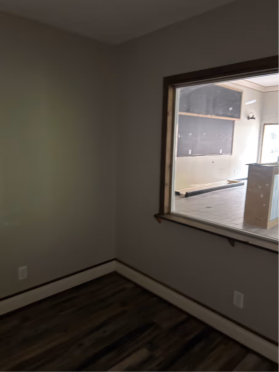 Interior office room before renovation with neutral walls, wood look flooring, and interior observation window.