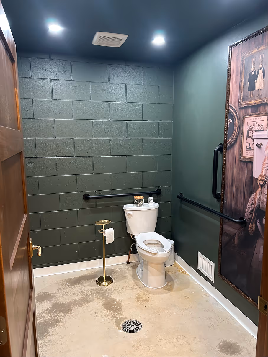 Accessible restroom with toilet, grab bars, green painted walls, and polished concrete flooring.