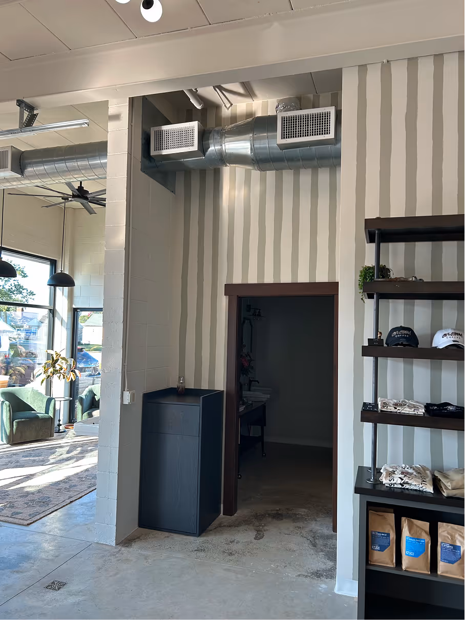 Retail display shelving with folded apparel, hats, striped accent wall, and adjacent doorways.