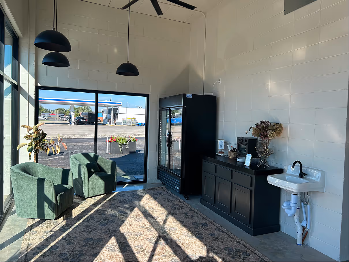 Seating area with two upholstered chairs, large windows, pendant lights, and polished concrete flooring.