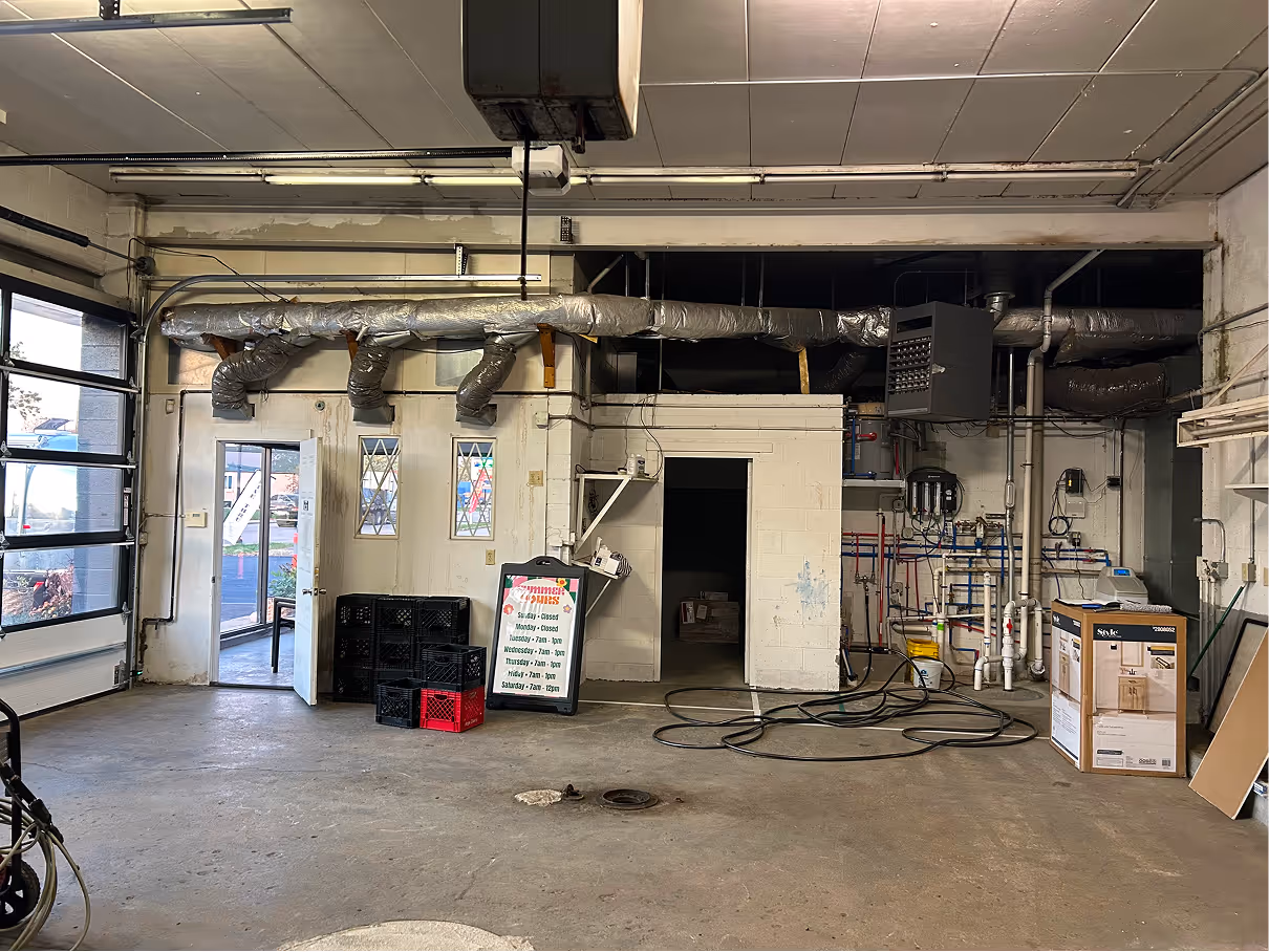 Wide view of unfinished commercial interior with overhead garage doors, exposed ceiling systems, and concrete floor.