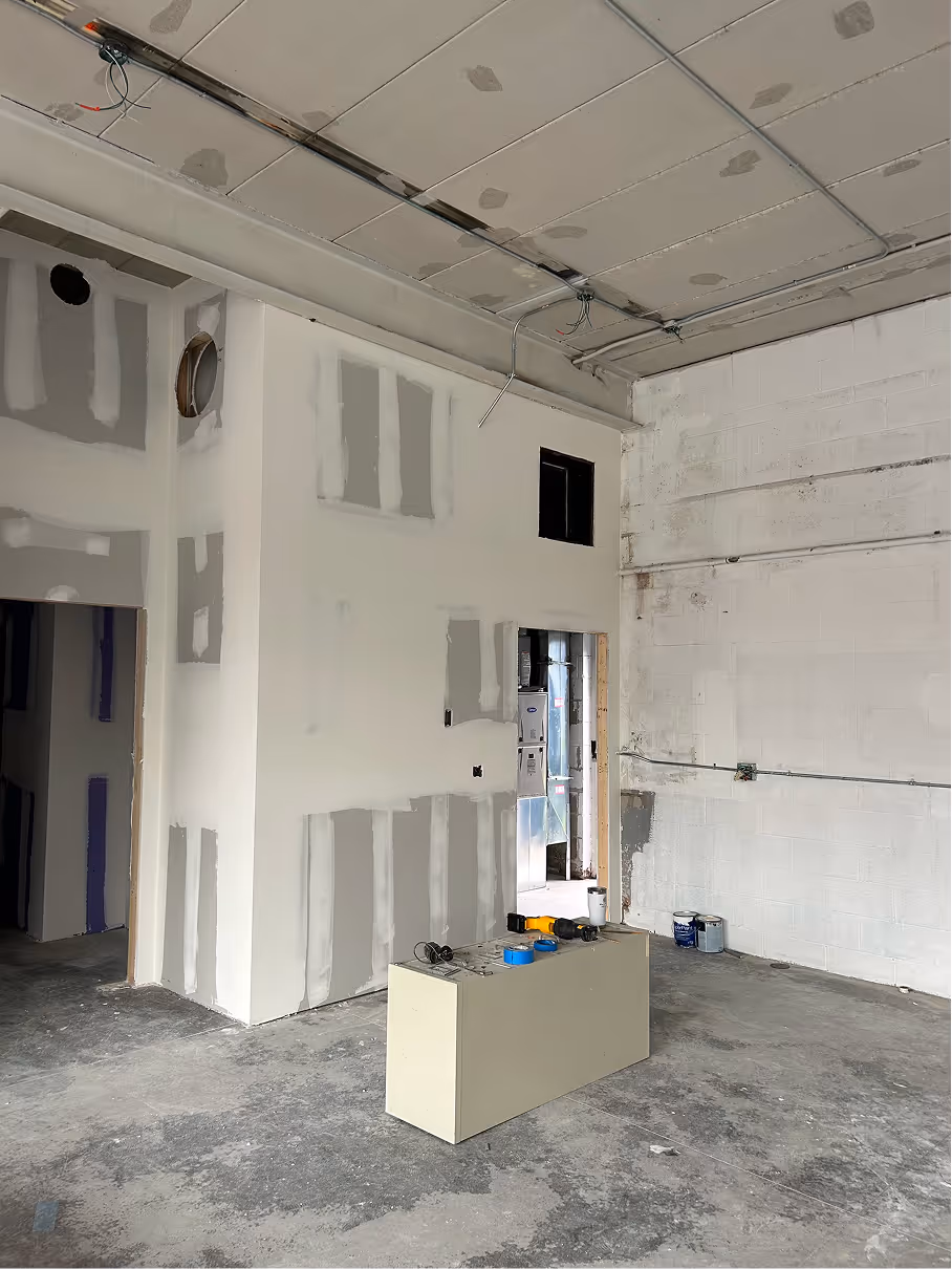 Interior room during renovation showing framed doorway, unfinished drywall, concrete floor, and exposed plumbing.