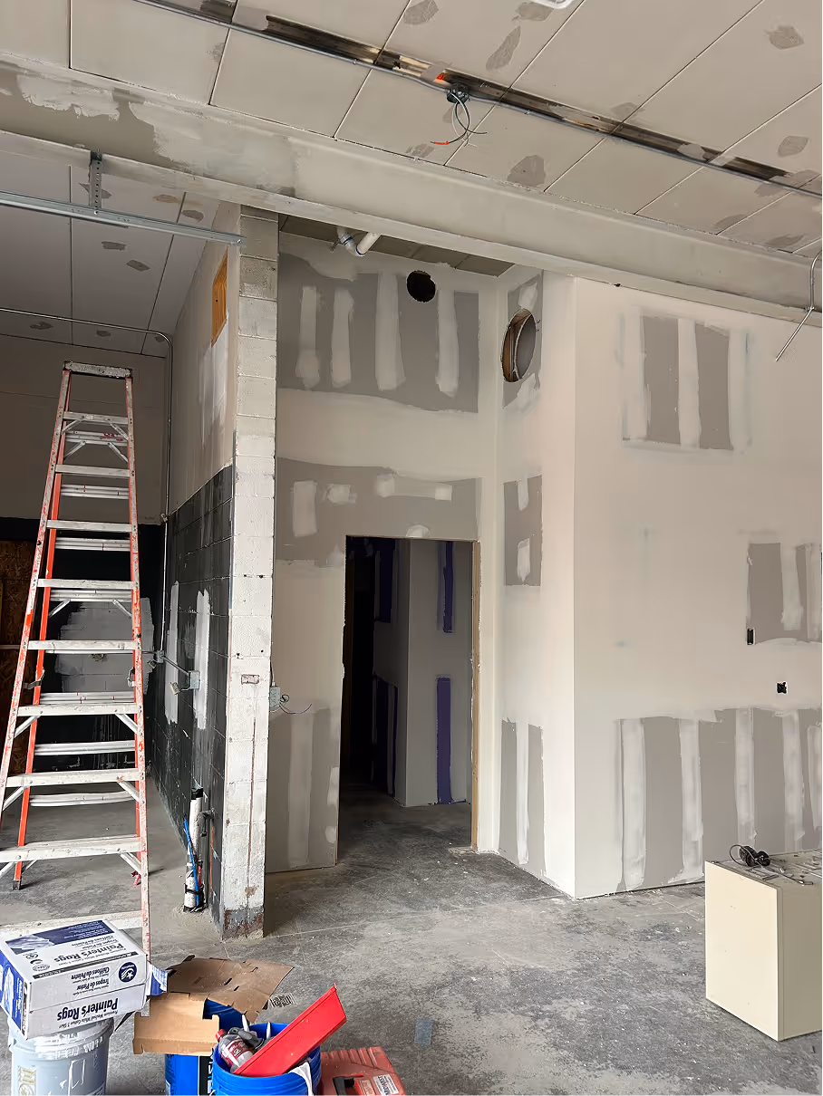Interior commercial renovation showing framed doorway, unfinished drywall, exposed ceiling, and ladder on concrete floor.