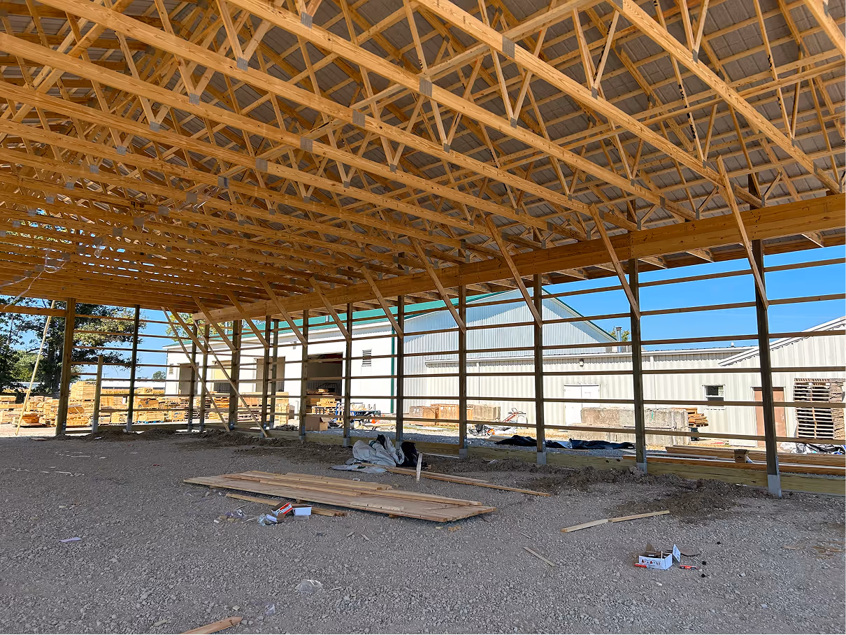 Side interior framing of post frame structure with open bays and lumber stacks.